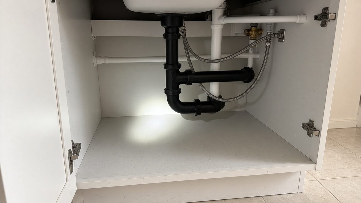 Flashlight inspection under a sink with plumbing pipes, a common cockroach harborage area